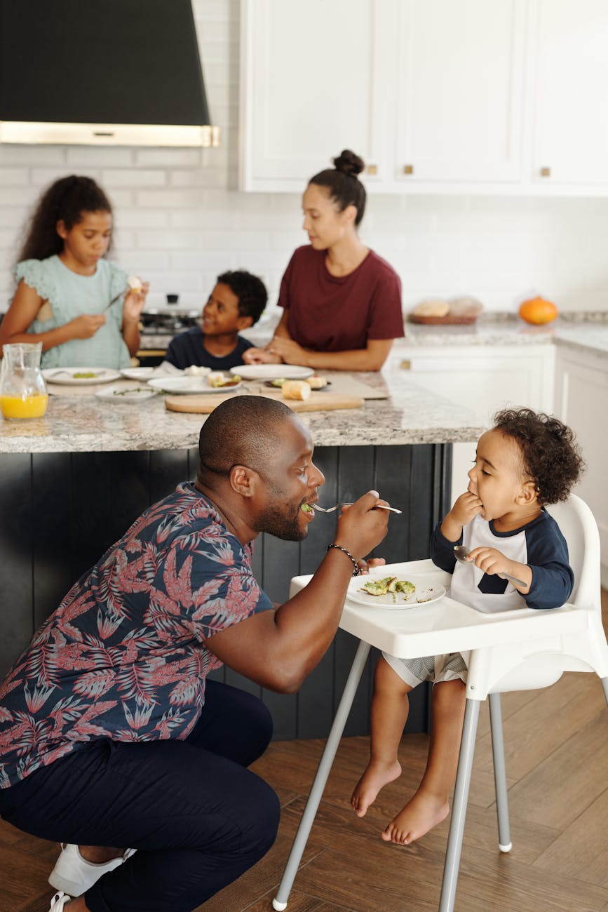 big family in kitchen and man feeding baby in feeding chair